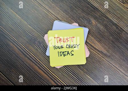 Concetto di fiducia le tue idee pazzo scrivere su note appiccicose isolato su tavola di legno. Foto Stock