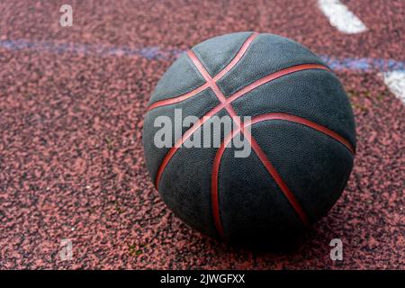 Palla da basket nera a terra. Primo piano sul campo rosso. Pallacanestro sulla strada o campo al coperto. Abbigliamento sportivo senza persone. Minimalismo. Foto Stock