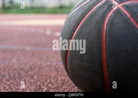 Palla da basket nera a terra. Primo piano sul campo rosso. Pallacanestro sulla strada o campo al coperto. Abbigliamento sportivo senza persone. Minimalismo. Foto Stock