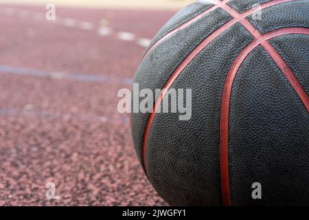 Palla da basket nera a terra. Primo piano sul campo rosso. Pallacanestro sulla strada o campo al coperto. Abbigliamento sportivo senza persone. Minimalismo. Foto Stock