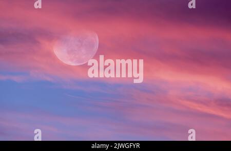 La Luna sta risplendente tra Un colorato cielo di Tramonto riempito di nube Foto Stock