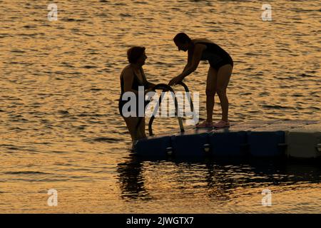 Due donne nuotano al tramonto sul Mar Egeo. Foto Stock