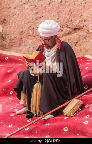 LALIBELA, ETIOPIA - 29 MARZO 2019: Sacerdote cristiano che legge un libro santo di fronte a Bet Maryam, chiesa di Lalibela, Etiopia Foto Stock