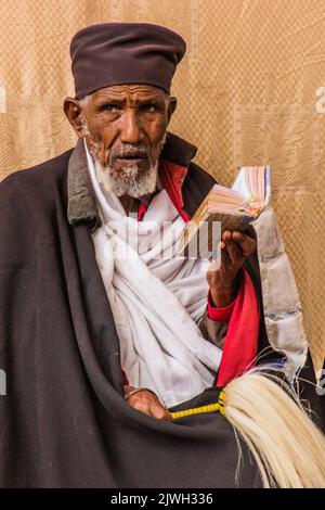 LALIBELA, ETIOPIA - 29 MARZO 2019: Sacerdote cristiano che legge una Bibbia di fronte a Bet Maryam, chiesa di Lalibela, Etiopia Foto Stock