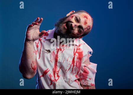 Zooky Halloween zombie guardare male pazzo, avendo sangue su camicia e pericoloso aggressivo sanguinoso look. Cadavere apocalittico inquietante con cicatrici e ferite sporche brutte, cervello che mangia demone. Foto Stock