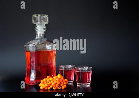 Liquore di Rowan, alcol forte fatto in casa e un mazzo di frutti di bosco maturi su sfondo nero. Primo piano. Foto Stock