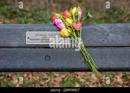 Un mazzo di fiori sono lasciati legati ad una panchina con una targa dedicata ad una recente morte in un parco nel Regno Unito di Londra del Nord Foto Stock