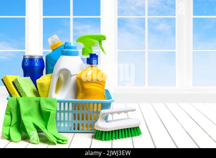Forniture per la pulizia della casa in cestello di plastica sul tavolo bianco sopra la finestra e cielo sfondo Foto Stock