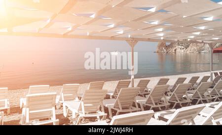 Sedie a sdraio vuote sotto un baldacchino sulla spiaggia. La spiaggia è vuota. Nessuna gente. Lettini in plastica bianca sotto il parasole. La stagione natalizia termina Foto Stock