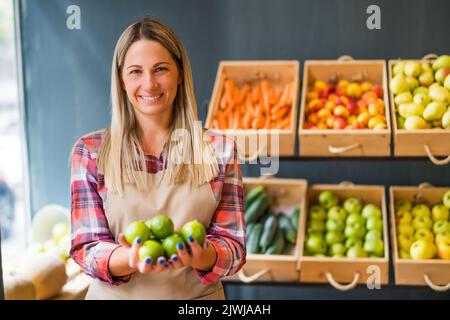 Donna lavora nel negozio di frutta e verdura. Sta tenendo la frutta del lime. Foto Stock
