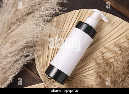 Cosmetic una bottiglia della pompa sulla foglia di palma asciutta vicino alla vista superiore dell'erba del pampas, mockup dell'etichetta. Prodotti di bellezza per la cura della pelle, lozione o essenza. Eco-friendly bohémien Foto Stock