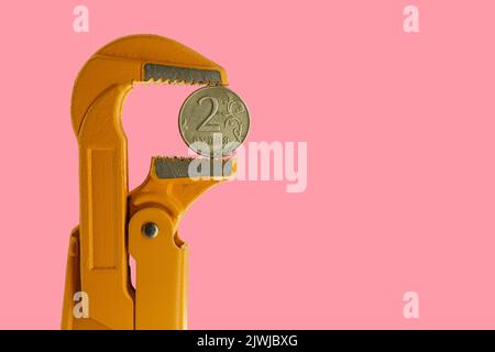 Moneta russa a due rubli tenuta in una chiave per idraulico arancione su uno sfondo rosa. Invertire il lato della moneta. Foto Stock