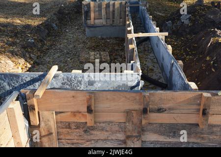 Un primo piano delle forme del legno di calcestruzzo, telaio di legno mentre costruisce una fondazione di calcestruzzo, basamento di striscia. Calcestruzzo che forma con forme di legno. Foto Stock