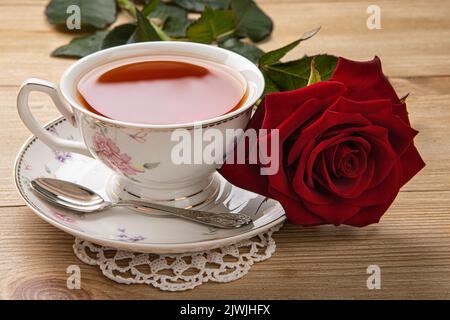 concetto di colazione: una tazza di tè e una rosa rossa sul tavolo Foto Stock