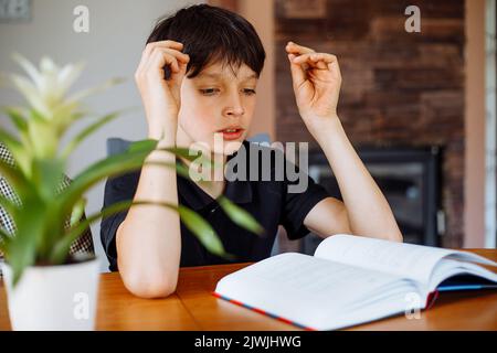 Teenager dai capelli scuri, libro di lettura dello studente a casa. Istruzione e studio. Imparare nuove informazioni, acquisire conoscenze. Esami Foto Stock