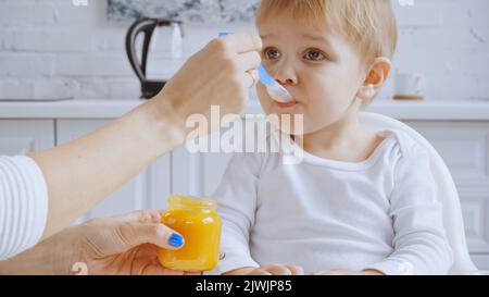 cucchiaio per la madre e bimbo che allatta con purea di carote nella sedia per l'allattamento Foto Stock