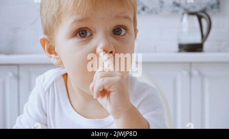 primo piano del bambino che picchietta il naso mentre guarda la fotocamera a casa Foto Stock