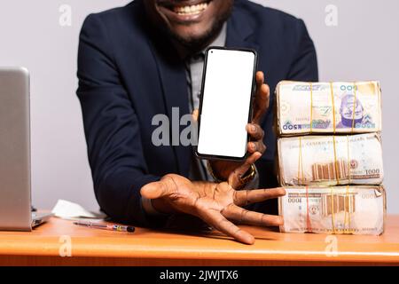 l'uomo nero eccitato mostra il suo schermo del telefono vicino a soldi molto Foto Stock
