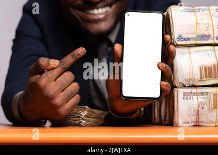 uomo africano che mostra il suo schermo del telefono accanto a un sacco di soldi Foto Stock