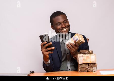 felice uomo d'affari africano con un sacco di soldi utilizzando un telefono Foto Stock