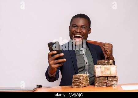 felice uomo d'affari africano con un sacco di soldi utilizzando un telefono Foto Stock