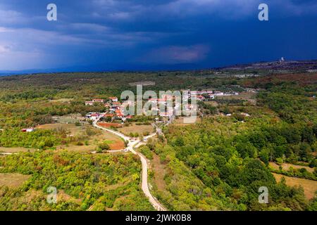 Vista aerea di un bellissimo piccolo villaggio, tradizionale villaggio carsico nella zona di Komen, in un giorno d'estate soleggiato, poco prima della tempesta, in Slovenia Foto Stock