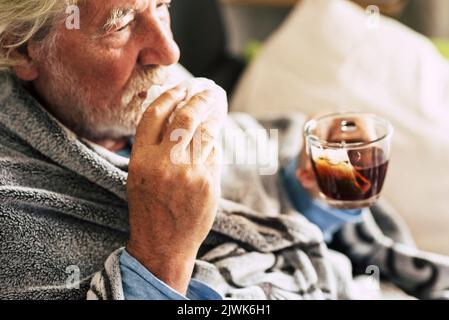 Un anziano con influenza fredda sintomi influenzali bere medicina o tè alle erbe naturale a casa per guarire. Concetto di virus e peopl anziano maturo Foto Stock