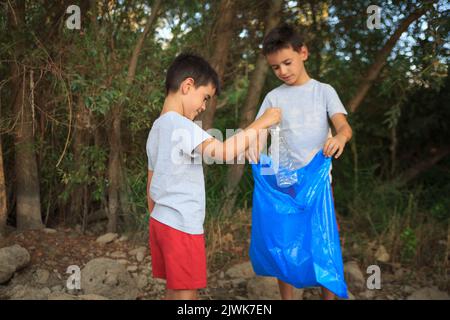 due bambini raccolgono rifiuti nella foresta. Educazione al riciclaggio e alla cura della natura Foto Stock