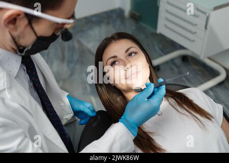 Vista sulla spalla di un medico dentista che tratta pazienti di sesso femminile. Donna che ha controllo dentale di routine presso il dentista. Foto Stock