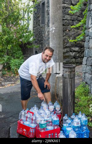 Riempire le bottiglie d'acqua con una deliziosa acqua potabile proveniente da una fontana pubblica nel villaggio siciliano di Milo, sulle pendici dell'Etna Foto Stock