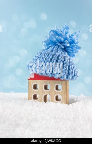 Figura di casa e abiti caldi sulla neve contro luci sfocate. Concetto di stagione di riscaldamento. Concetto europeo di crisi energetica. Spazio di copia. Foto Stock