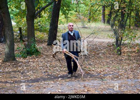 Un uomo allegro anziano pulisce il parco forestale da branches.Cets legna da ardere Foto Stock