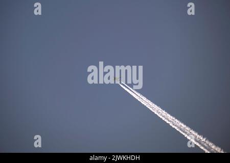 Aereo a getto di passeggeri distante che vola ad alta quota su cielo blu chiaro lasciando dietro una traccia di fumo bianco di contrail. Concetto di trasporto aereo Foto Stock