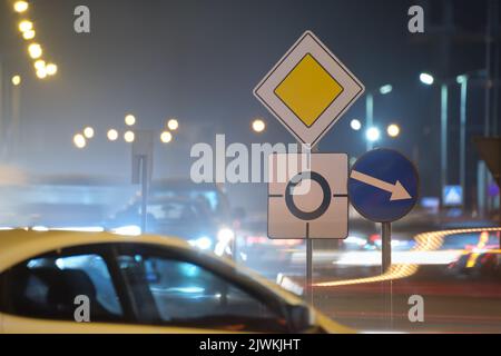 Segnaletica stradale rotonda con auto sfocate sul traffico stradale cittadino di notte. Concetto di trasporto urbano Foto Stock