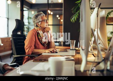 Donna d'affari matura che lavora su un computer in un ambiente di lavoro moderno. Donna d'affari con esperienza che lavora in un co-ufficio. Foto Stock