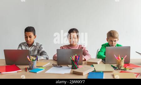 Tre ragazzi della scuola multirazziale che usano i laptop che imparano in linea alla scuola Foto Stock