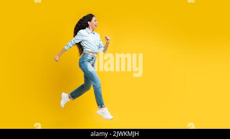 Gioiosa Signora araba che corre a mezz'aria su sfondo giallo Foto Stock
