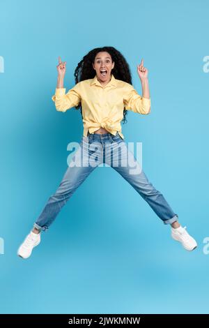 Gioioso arabo femmina saltando le dita di puntamento su su sfondo blu Foto Stock