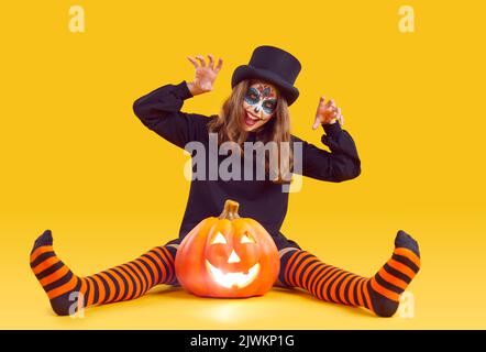 Allegra ragazza pre con trucco di Halloween fa graffiare il gesto su sfondo arancione. Foto Stock