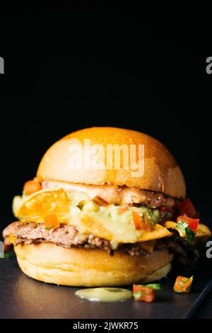 Doble hamburger con nachos, pomodori tritati e salsa di guacamole su sfondo nero Foto Stock