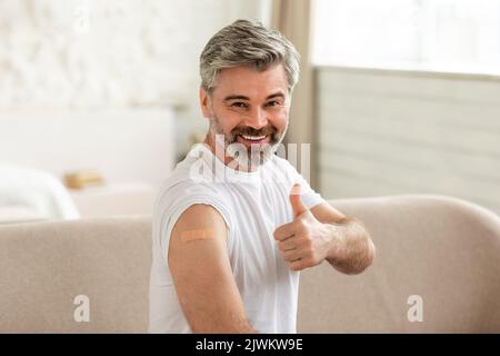 Allegro vaccinato maschio mostrando braccio e gesturing pollice in su interno Foto Stock