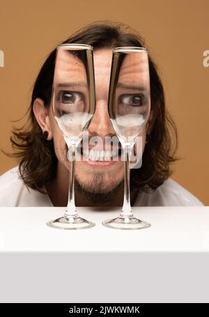 Faccia felice dell'uomo attraverso i bicchieri del vino. Distorsione degli oggetti, illusione ottica. Arte contemporanea minimalista Foto Stock