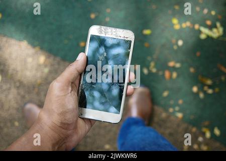 Primo piano della mano dell'uomo che tiene in mano lo smartphone rotto. Foto Stock
