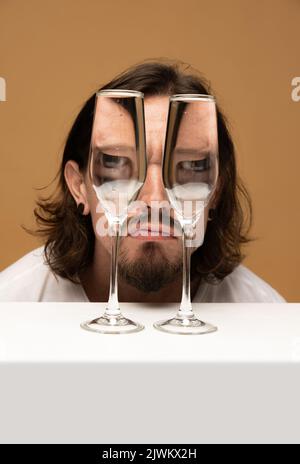 Faccia felice dell'uomo attraverso i bicchieri del vino. Distorsione degli oggetti, illusione ottica. Arte contemporanea minimalista Foto Stock