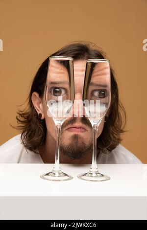 Faccia felice dell'uomo attraverso i bicchieri del vino. Distorsione degli oggetti, illusione ottica. Arte contemporanea minimalista Foto Stock