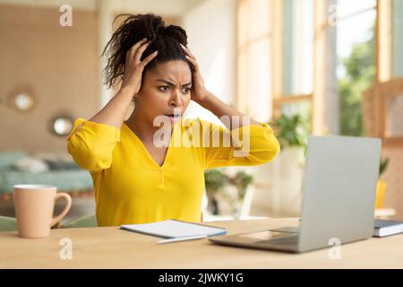 OH no, scioccante business news concetto. Emotiva afroamericana businesswoman guardando il notebook e toccando la testa Foto Stock