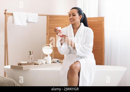 Donna che tiene aperto vaso idratante cura della pelle in bagno Foto Stock