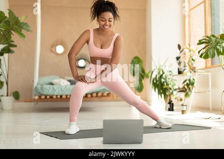 Donna sportiva che si esercita a casa, stretching le gambe, guardare tutorial online sul computer portatile o avere una classe di fitness online Foto Stock