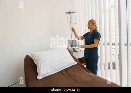 Infermiere professionista che prepara un'infusione endovenosa prima della procedura nel reparto ospedaliero Foto Stock