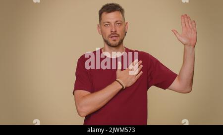 Giuro di essere onesto. Un giovane sincero e responsabile che alza la mano per fare giuramento, promettendo di essere onesto e di dire la verità, mantenendo la mano sul petto. Ragazzo di stile adulto isolato su sfondo beige Foto Stock